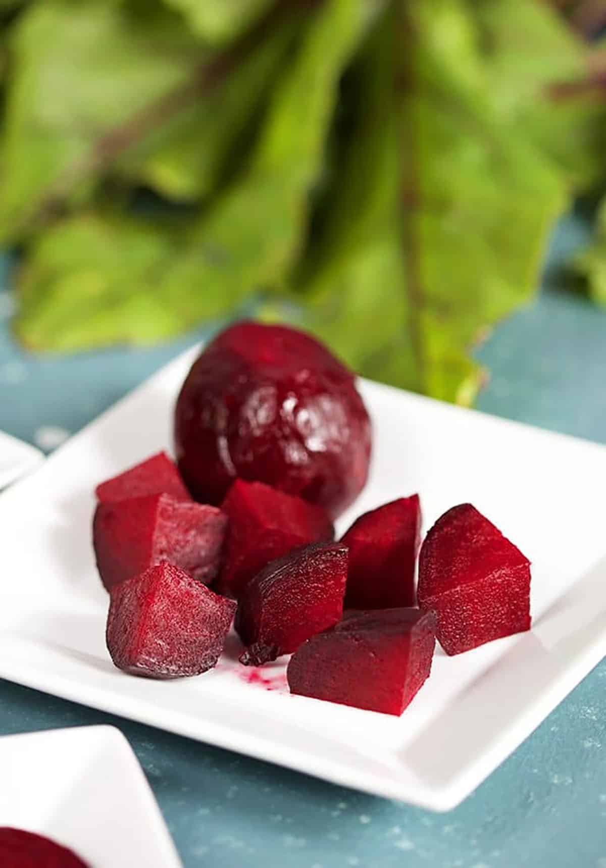 Diced Roasted Beets on a white square plate with beet greens in the background.