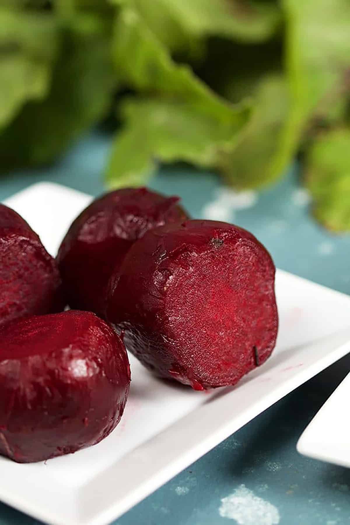 Oven Roasted Beets on a white square plate with beet greens in the background.