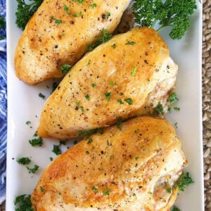 Three crispy roasted chicken breasts on a white rectangular platter.