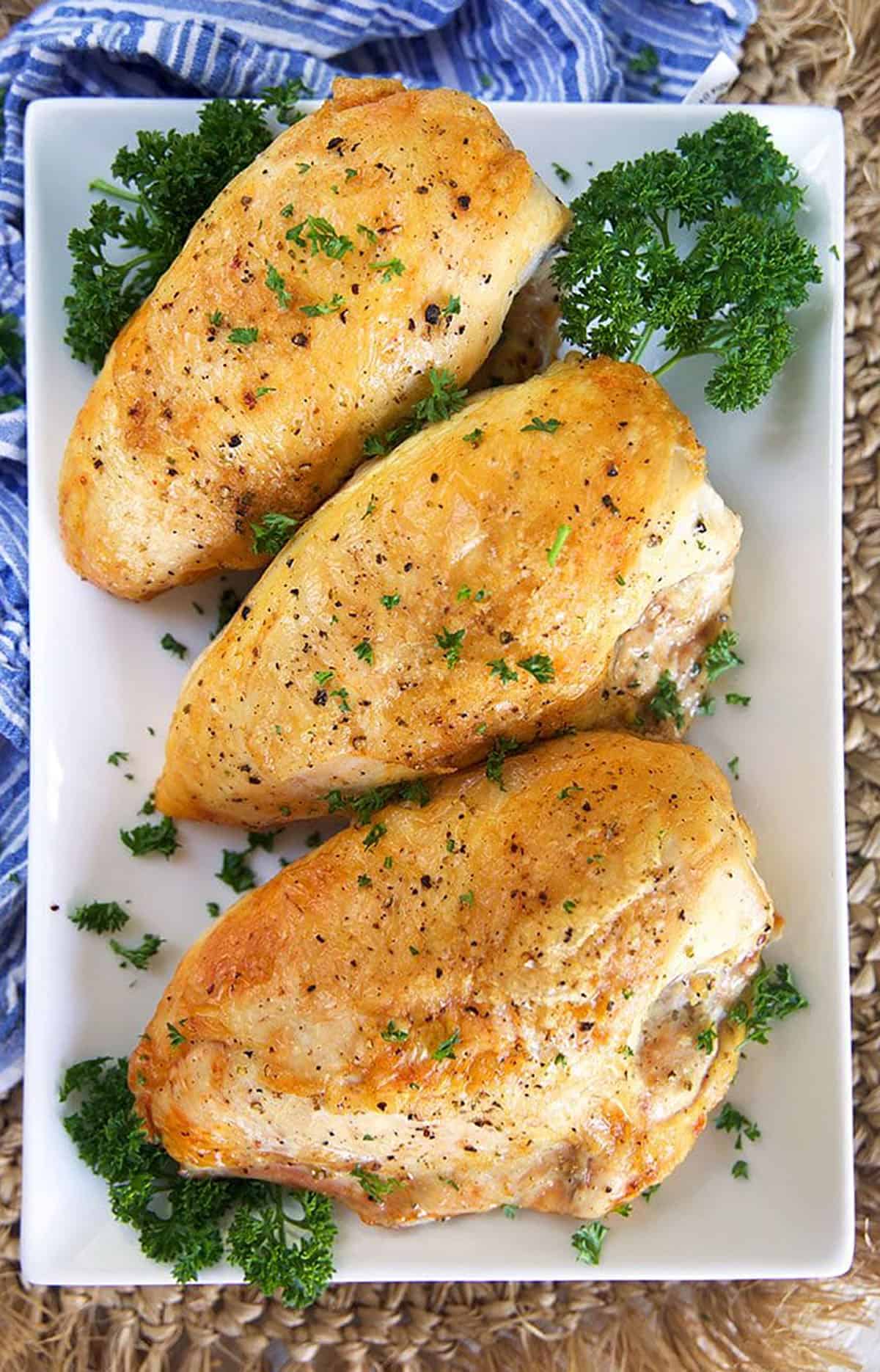 Three crispy roasted chicken breasts on a white rectangular platter.