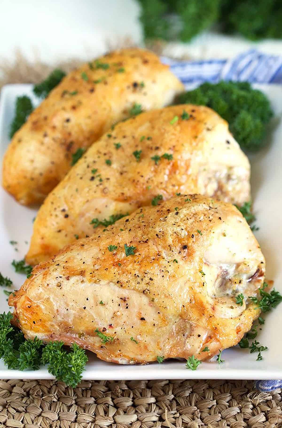 Golden crispy roasted chicken breasts on a white platter with parsley.