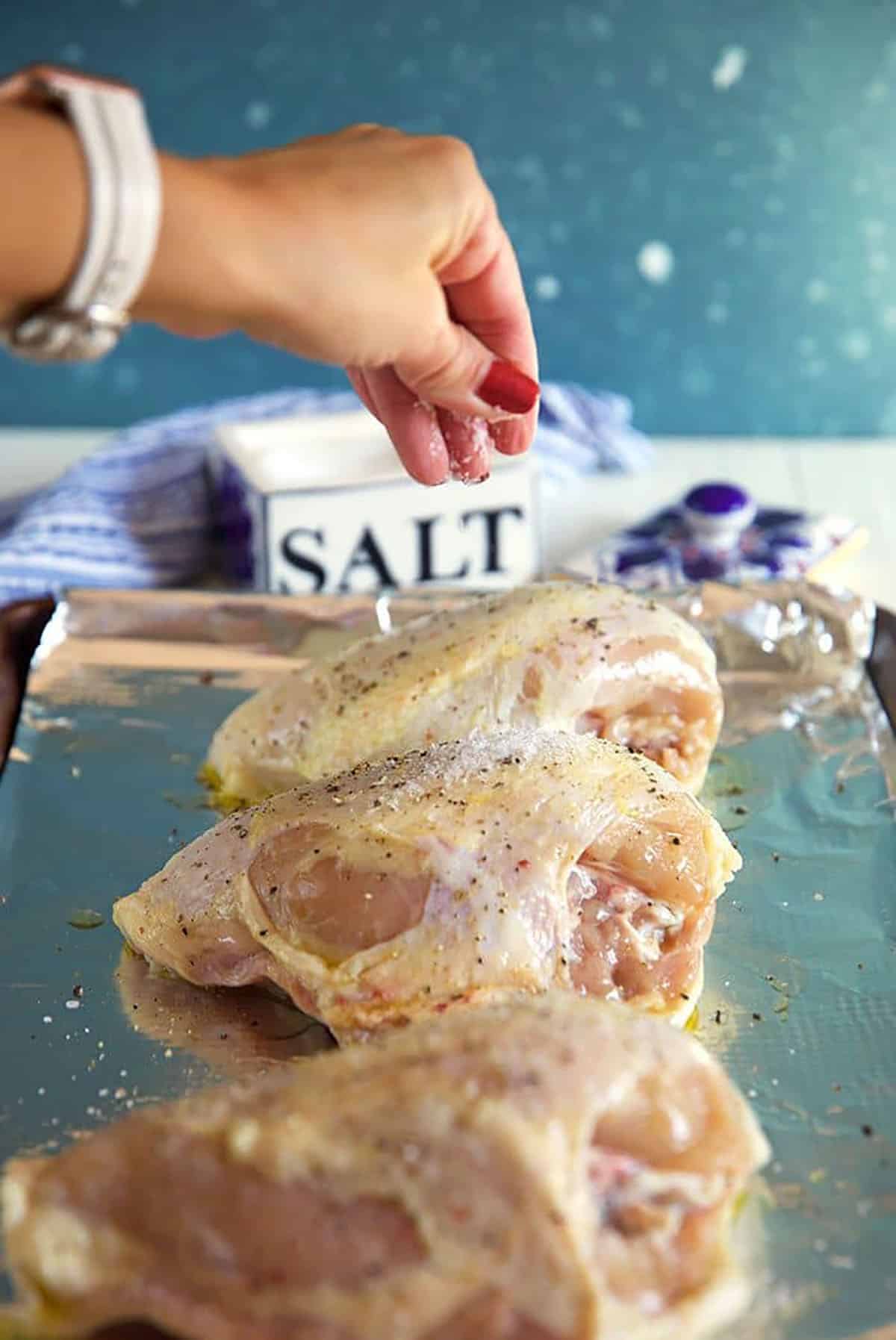 Salt being sprinkled on a bone in chicken breast.