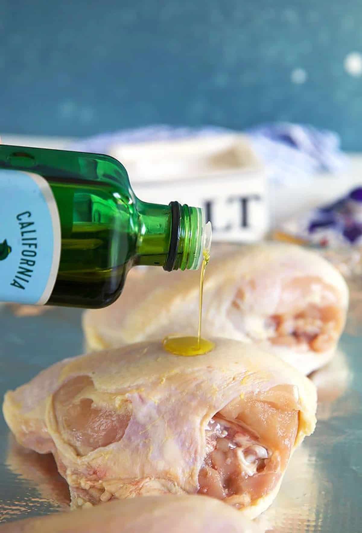 Olive oil being drizzled on a bone in skin on chicken breast.