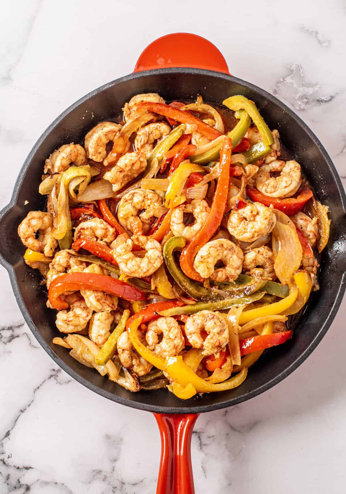 Shrimp and bell peppers are cooked in a large black and red skillet.