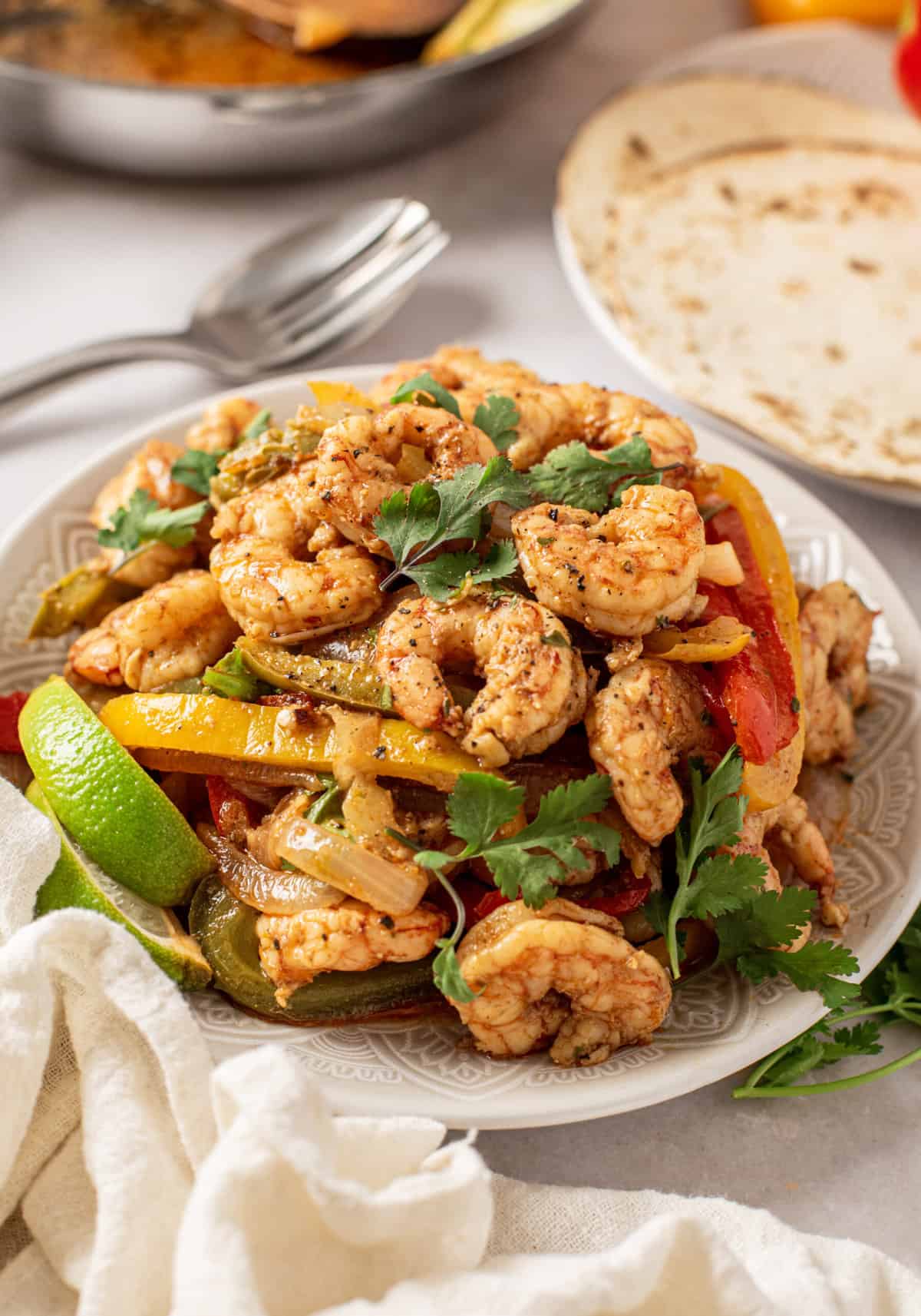 Shrimp fajitas are presented on a white plate with cilantro and a lime wedge.