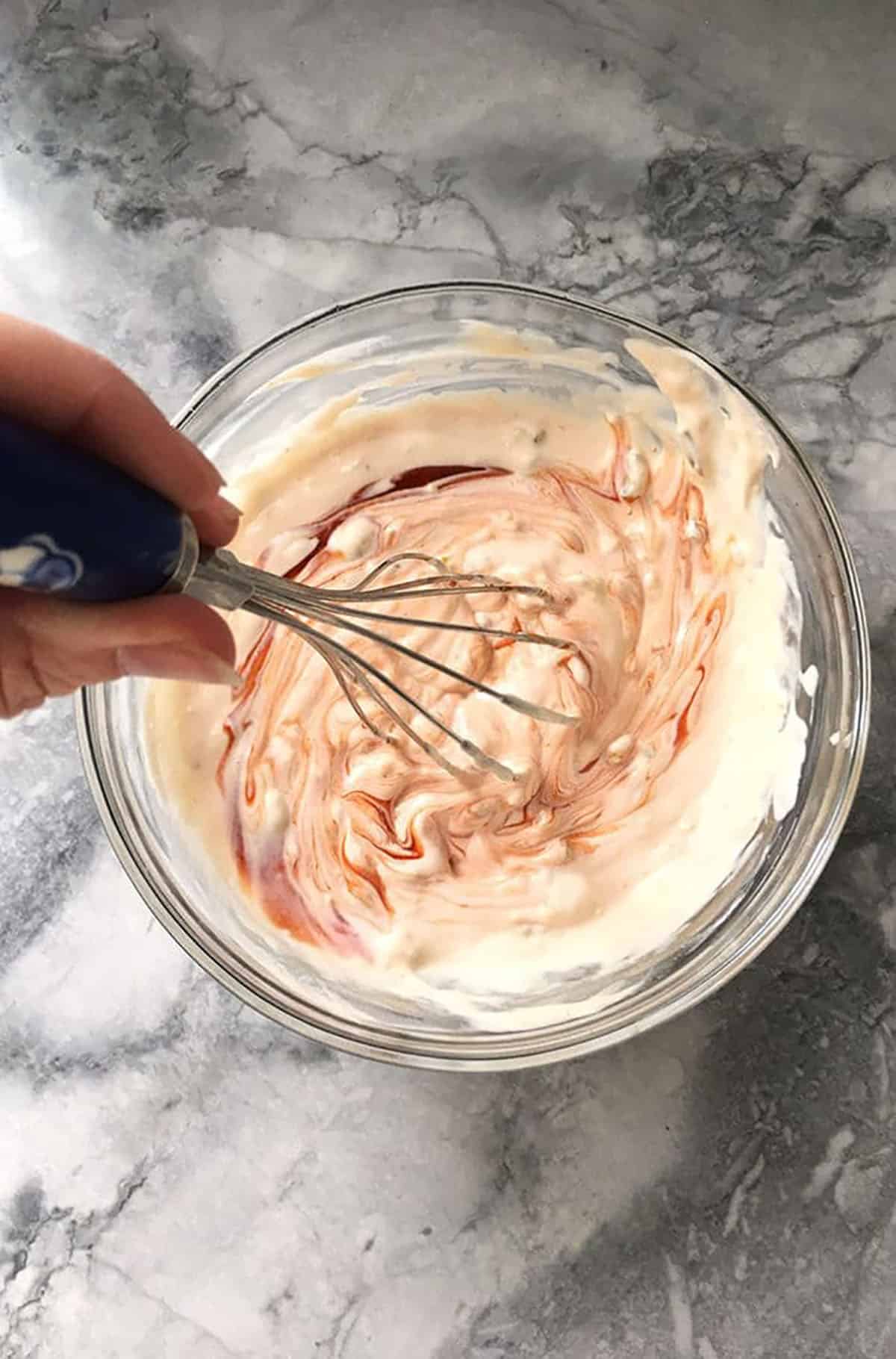 Thousand Island Dressing being whisked in a glass bowl with a whisk.