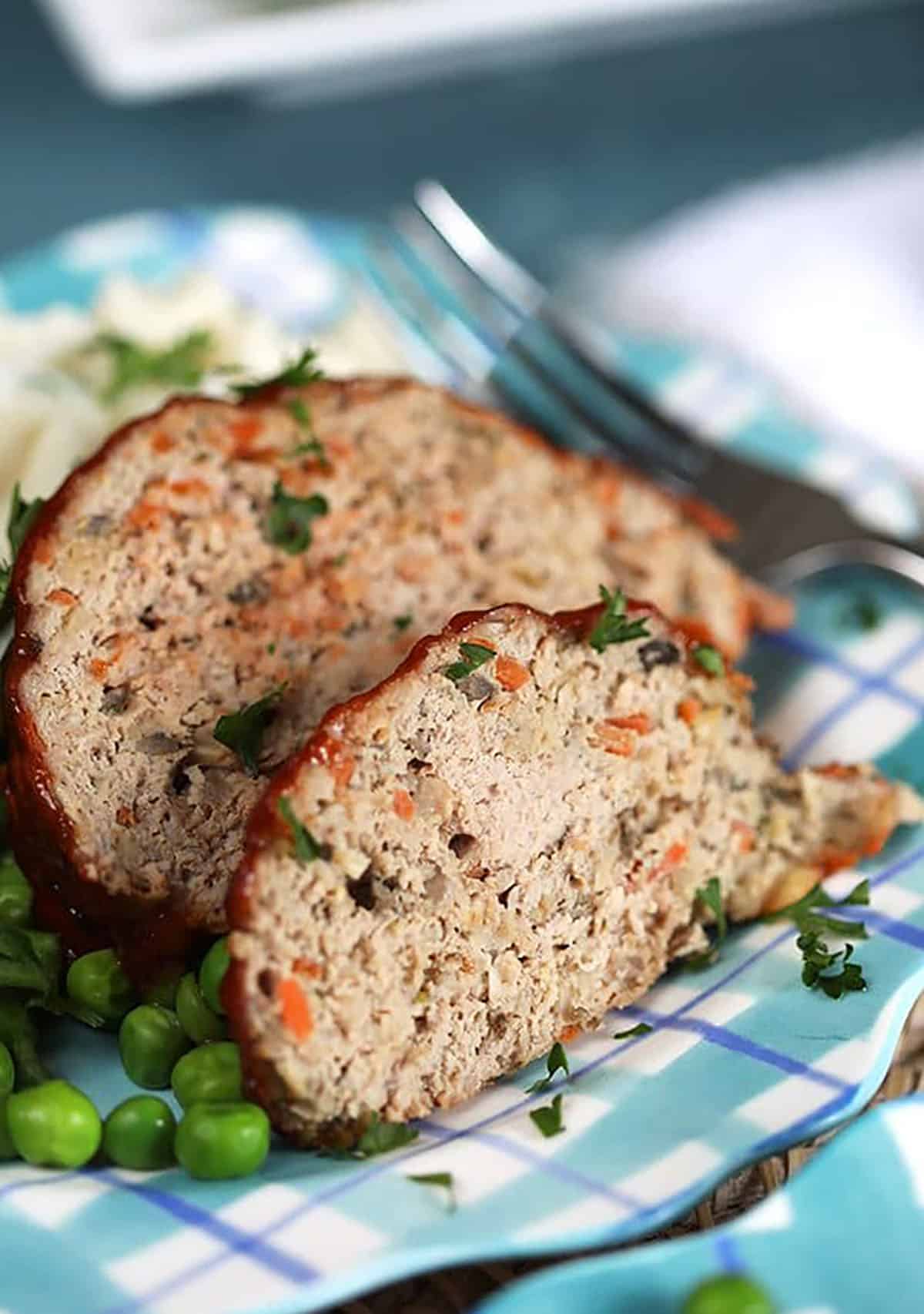 Two slices of Turkey Meatloaf on a plaid plate with mashed potatoes.