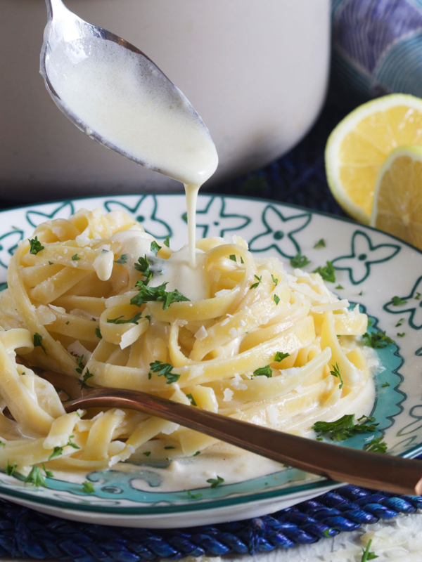 Alfredo sauce is being drizzled over pasta noodles.