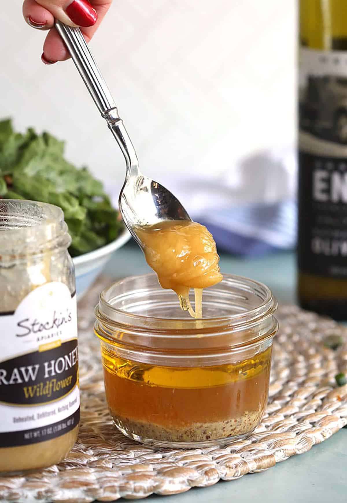 Honey being added to a glass jar to make apple cider vinaigrette.