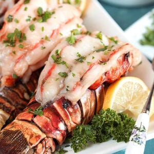 Baked lobster tails on a white platter with lemon and parsley.