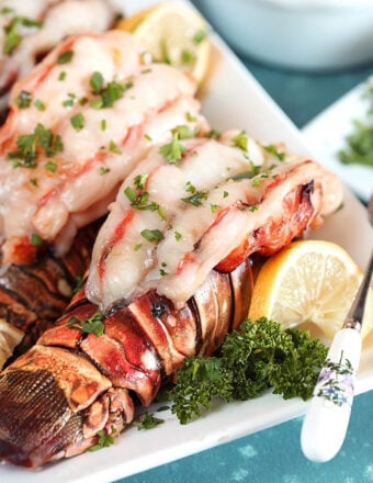 Baked lobster tails on a white platter with lemon and parsley.