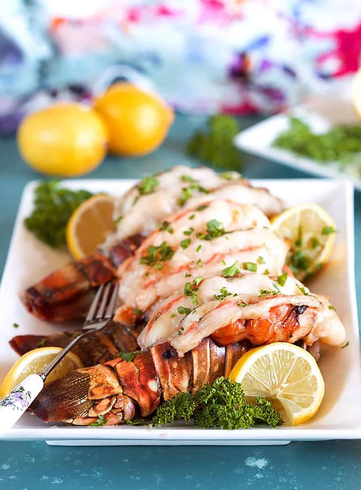 Baked lobster tail on a white platter with lemon and parlsey.