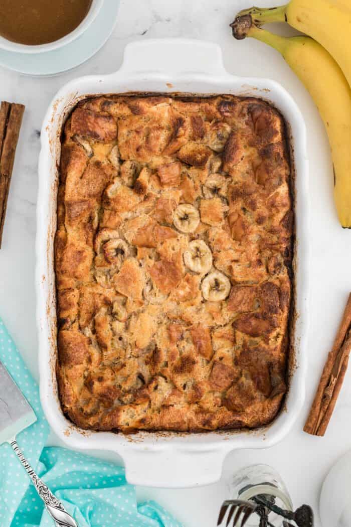 A white casserole dish is filled with baked banana bread pudding.