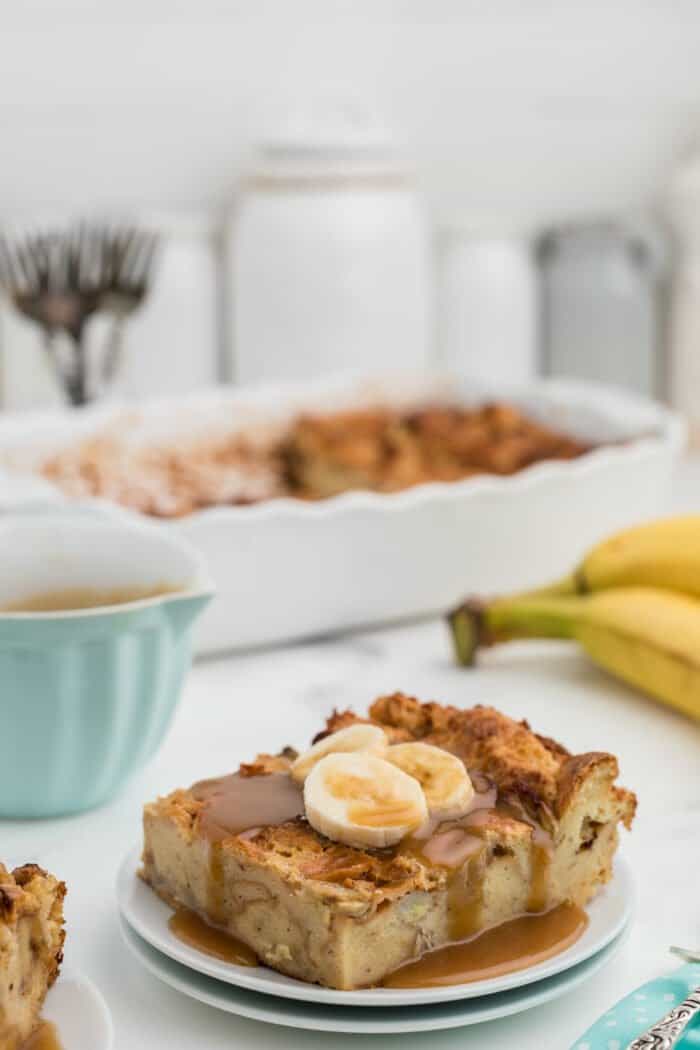 A plate with a slice of bread pudding is topped with caramel and banana slices.