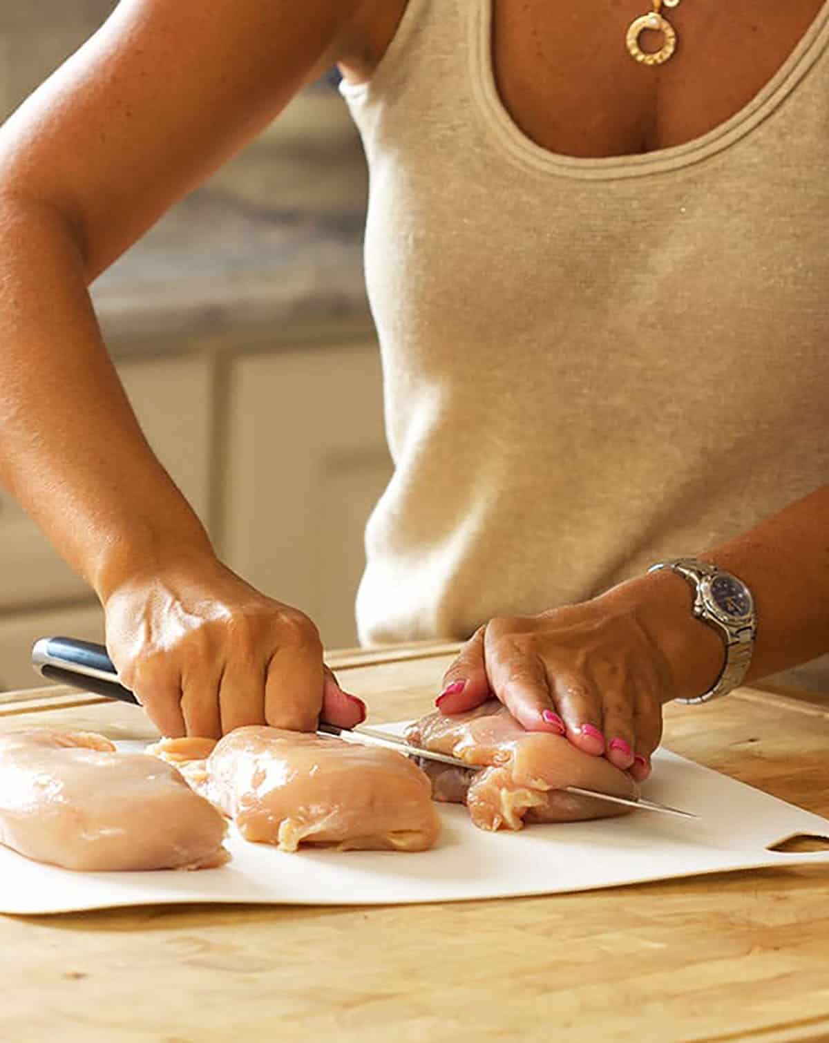 woman slicing chicken breast in half on a wooden countertop.