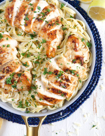A pan of sliced chicken breast and creamy fettuccine is presented on a blue place mat.