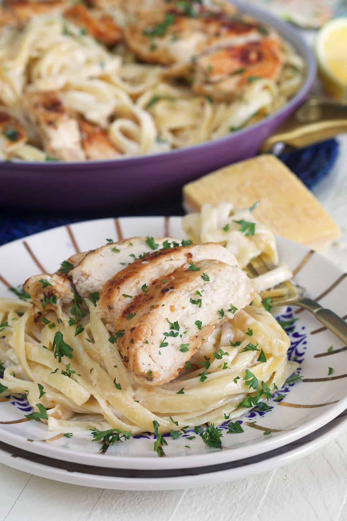 A striped plate is topped with a serving of chicken alfredo.