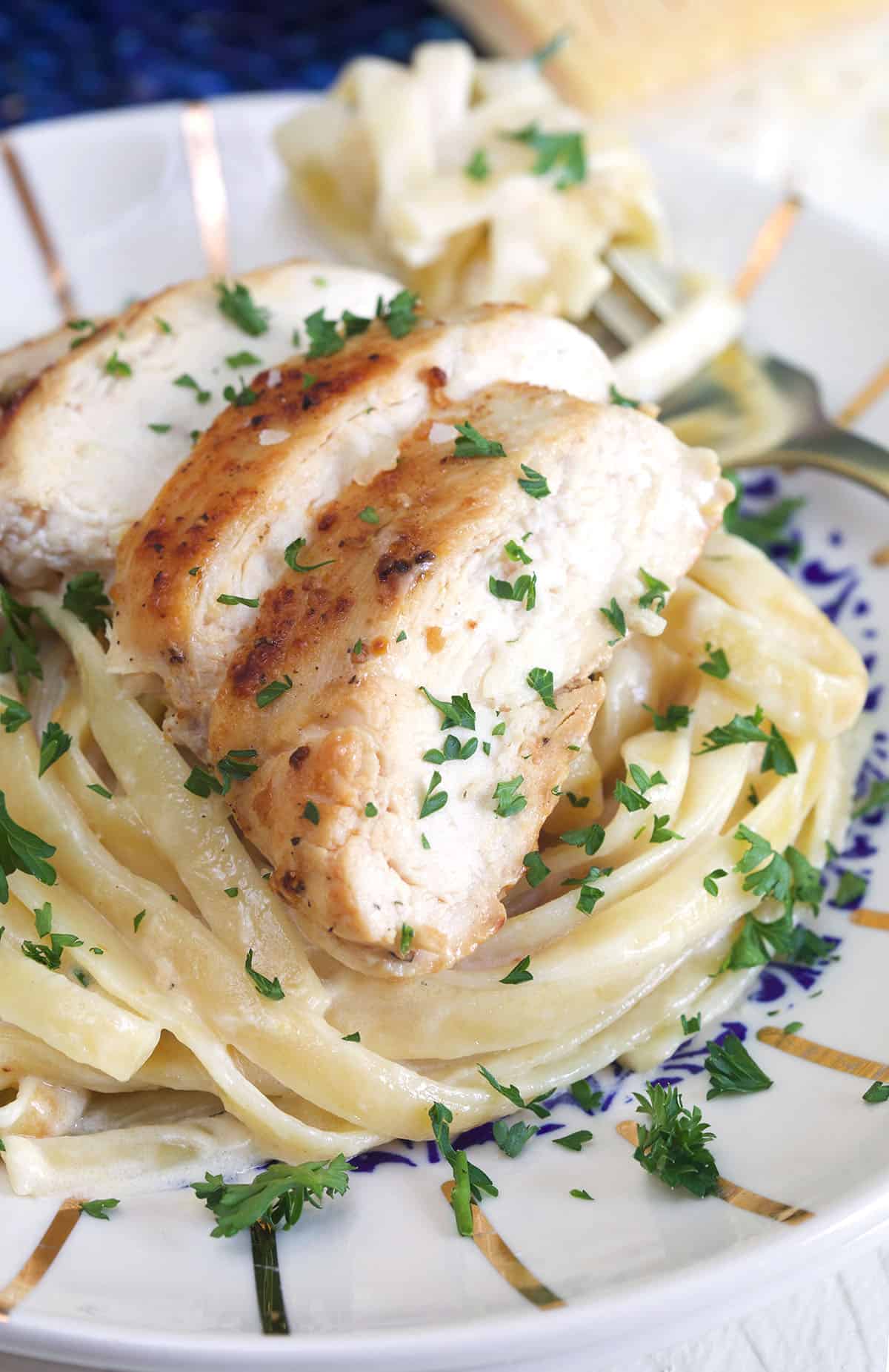 A pile of pasta is topped with cooked chicken breast slices.