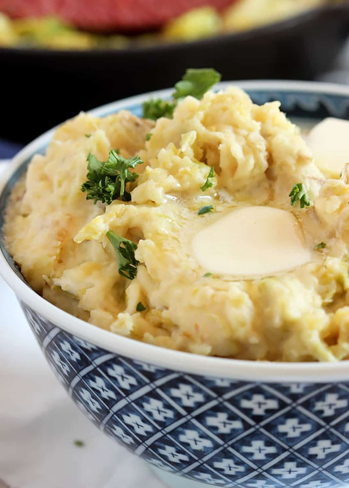 colcannon potatoes in a blue and white bowl with a pat of butter on top and sprinkled with parsley.