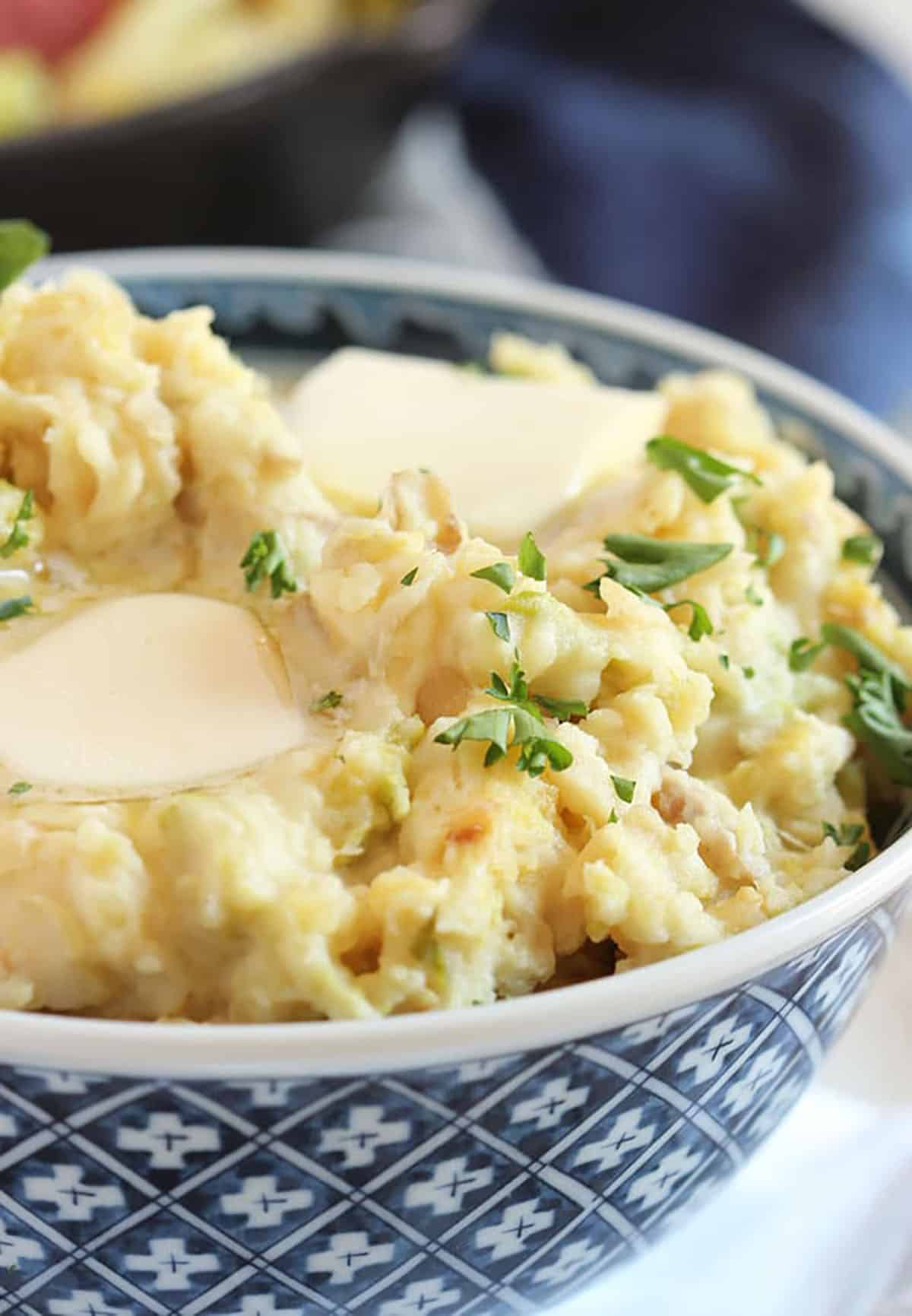 Colcannon potatoes in a blue and white bowl with melted butter on top.