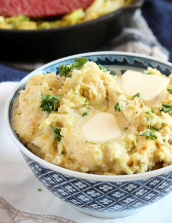Irish Colcannon Potatoes in a blue and white bowl with corned beef in the background.