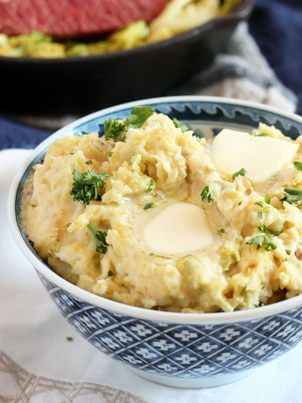 Irish Colcannon Potatoes in a blue and white bowl with corned beef in the background.