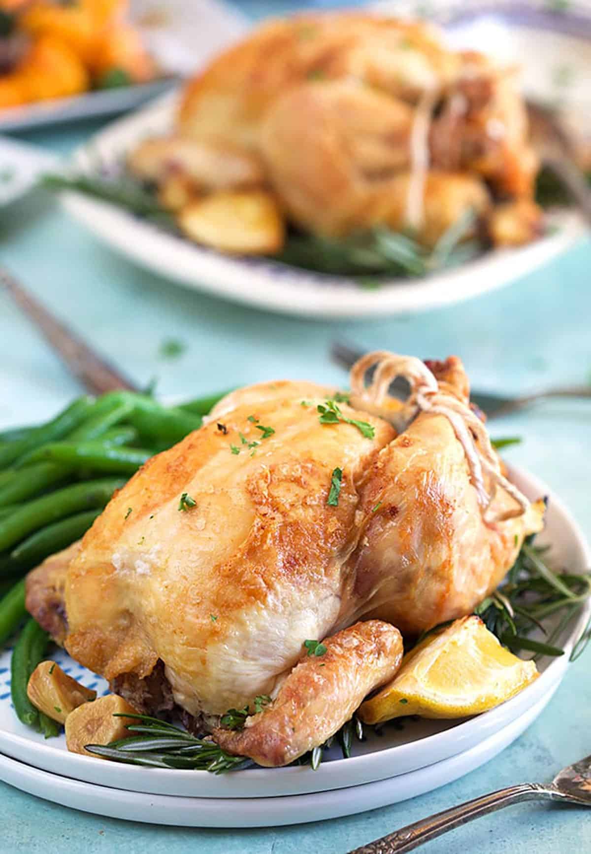 Cornish hen on a white plate with roasted lemon and green beans.