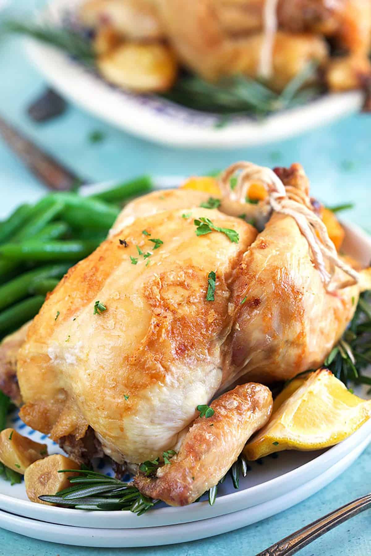 Close up of cornish hen on a white plate with a lemon wedge and green beans.