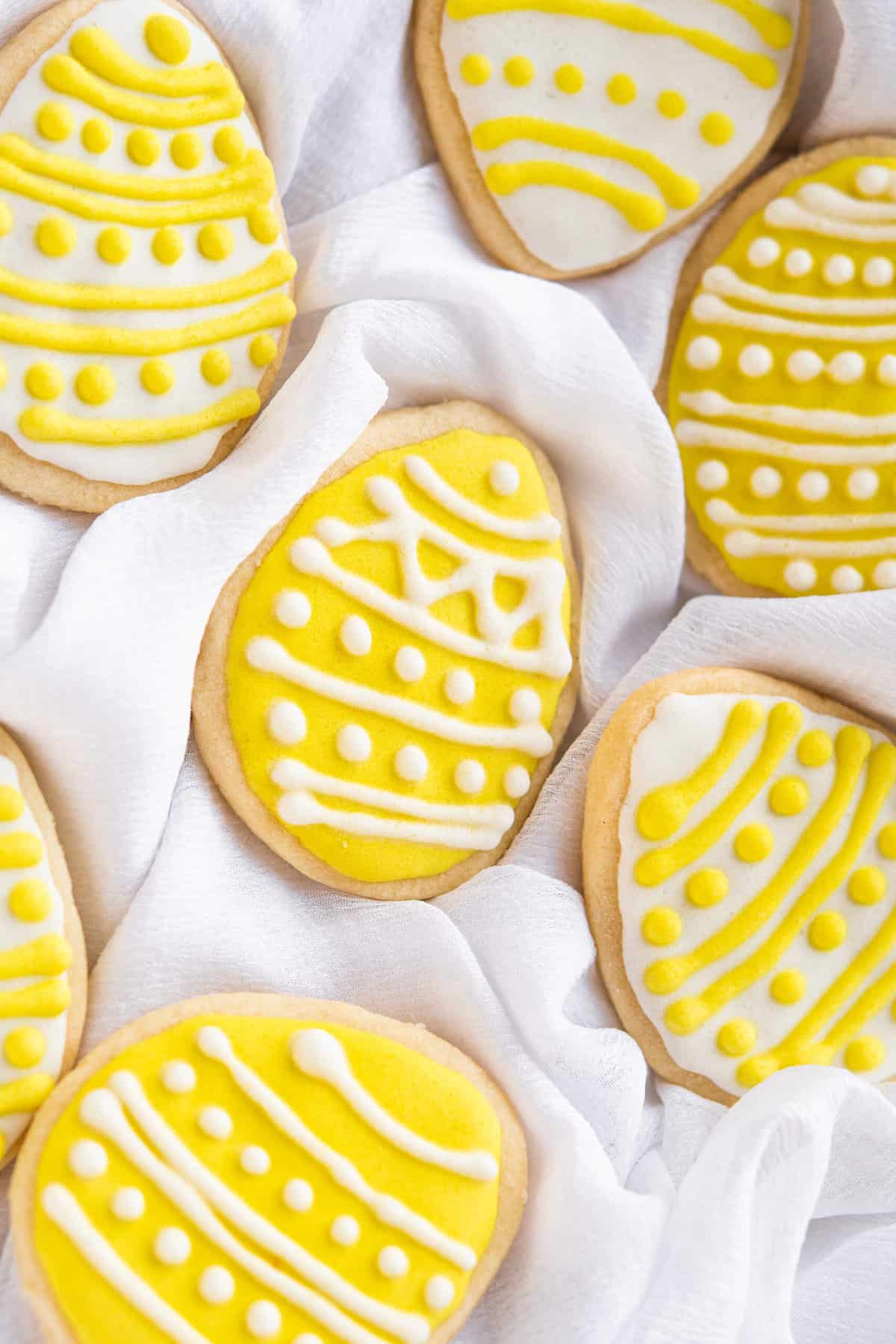 A few yellow and white easter cookies are placed on a gentle white tea towel.
