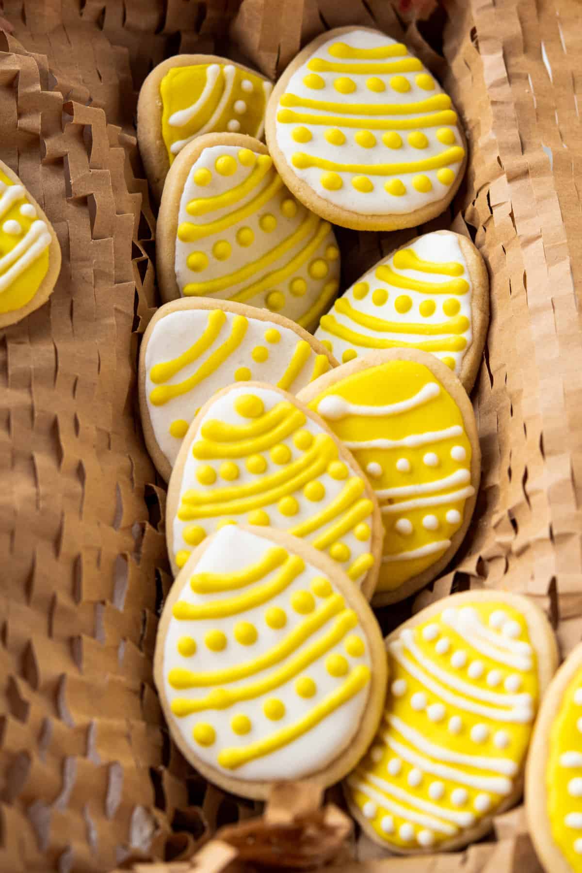 A batch of white and yellow easter egg sugar cookies are placed in a basket.