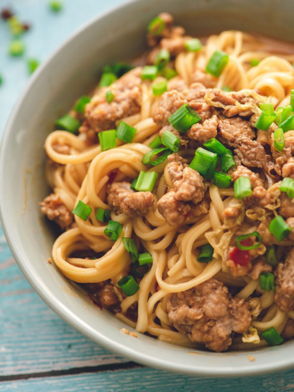 Dan Dan noodles in a gray bowl with chopped green onion on top.