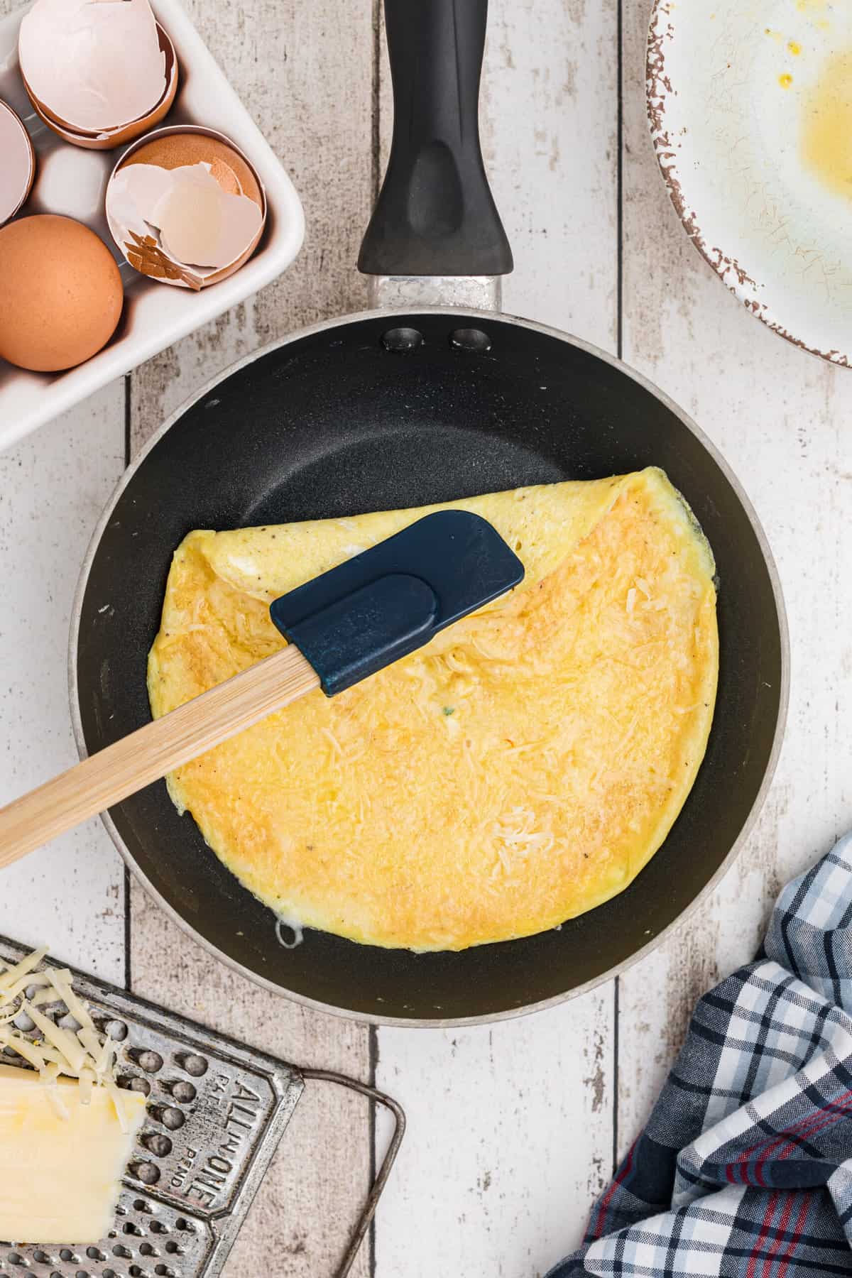 An omelette is beign gently rolled with a spatula in a pan.