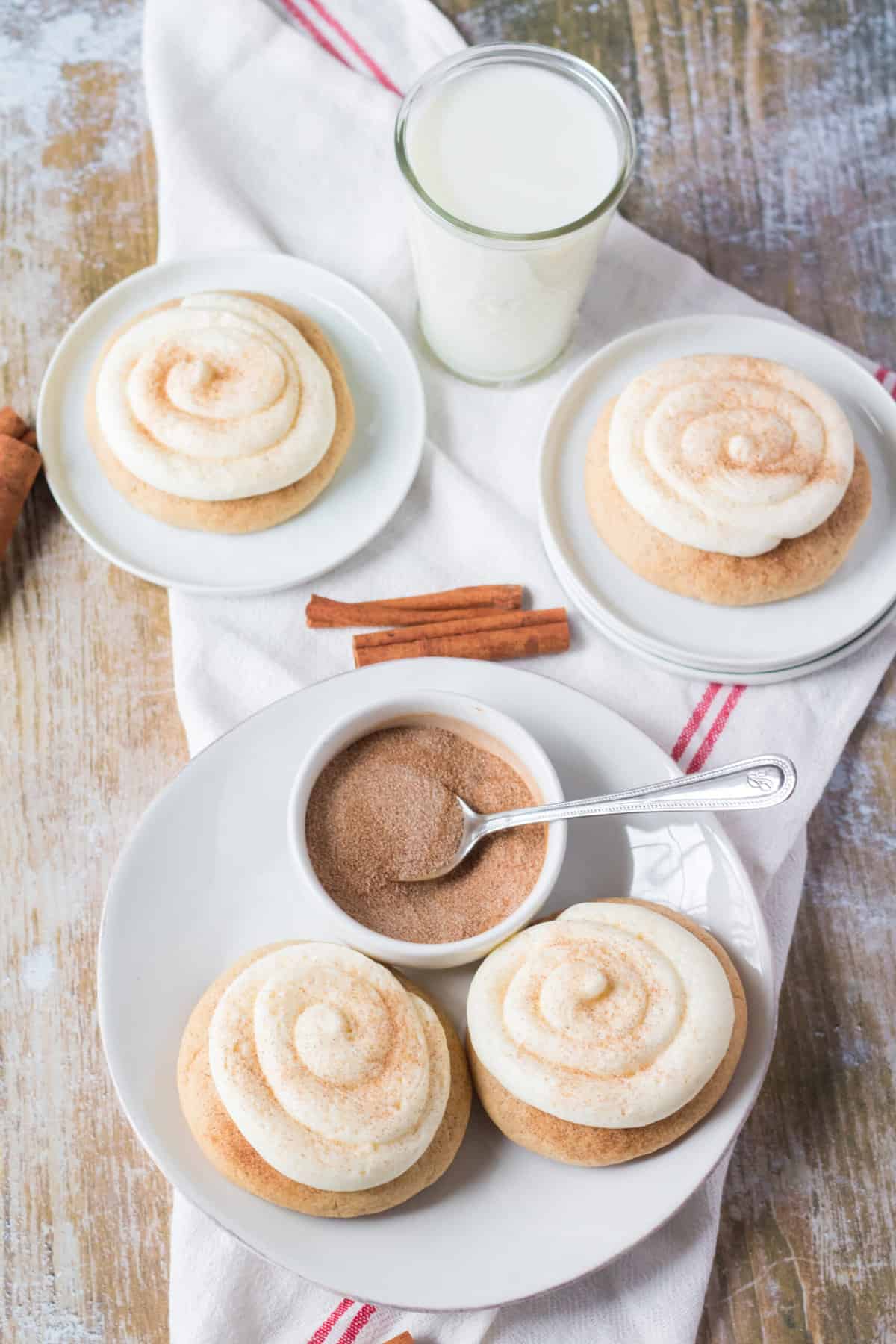 Frosted snickerdoodle cookies are placed next to an extra bowl of cinnamon sugar with a glass of milk.