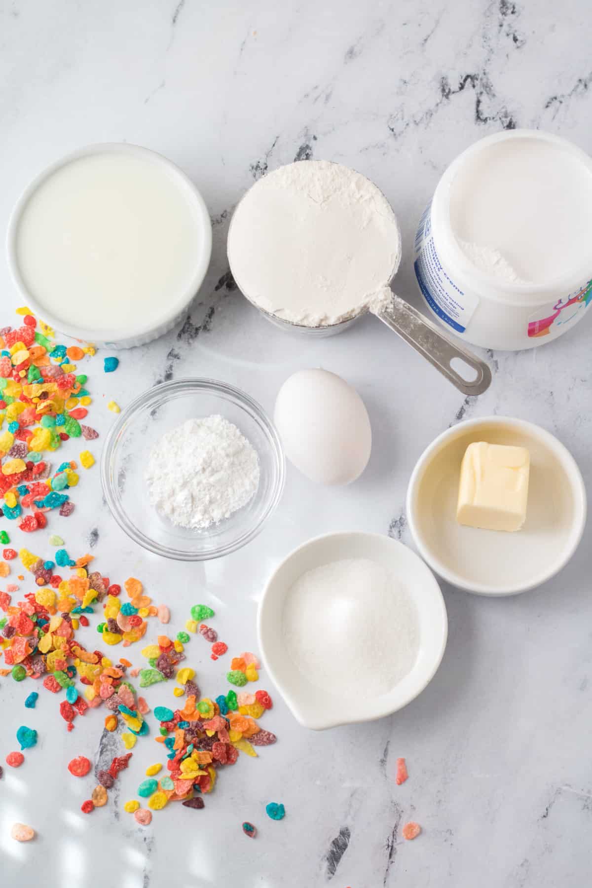 The ingredients for fruity pebbles pancakes are presented on a marble countertop. 