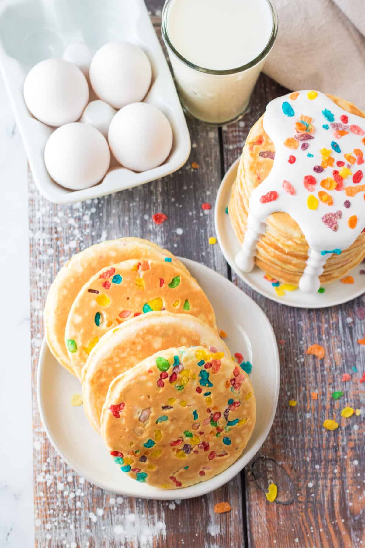 A carton of eggs is placed next to one stack of plain pancakes and another with marshmallow fluff.
