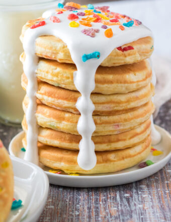A stack of panckes is drizzled with white marshmallow fluff and topped off with fruity pebbles.