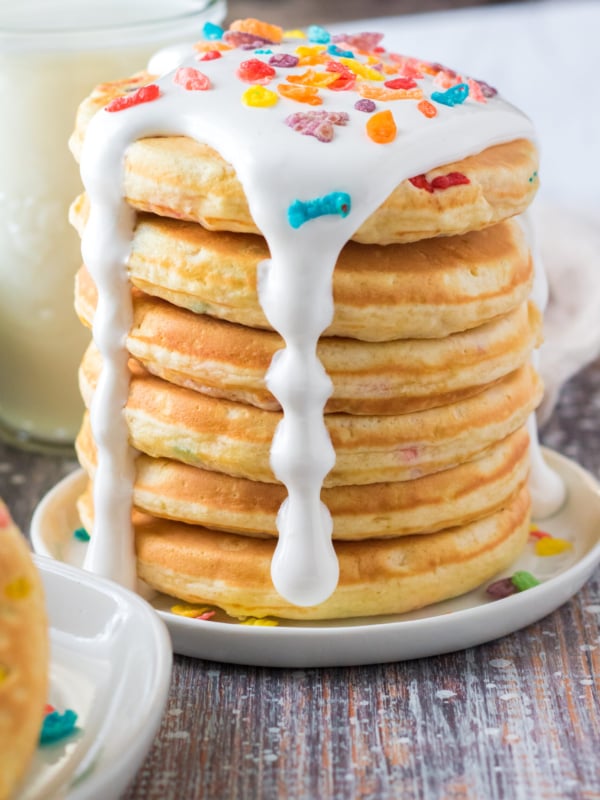 A stack of panckes is drizzled with white marshmallow fluff and topped off with fruity pebbles.