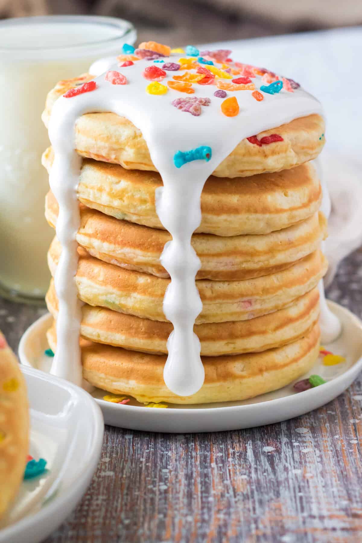 A stack of panckes is drizzled with white frosting and topped off with fruity pebbles.