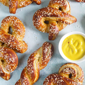 Soft pretzels on a blue background with yellow mustard in a white dish.