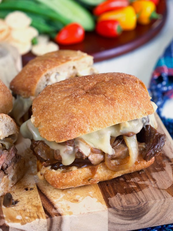 A halved roast beef sandwich is placed on a wooden cutting board.