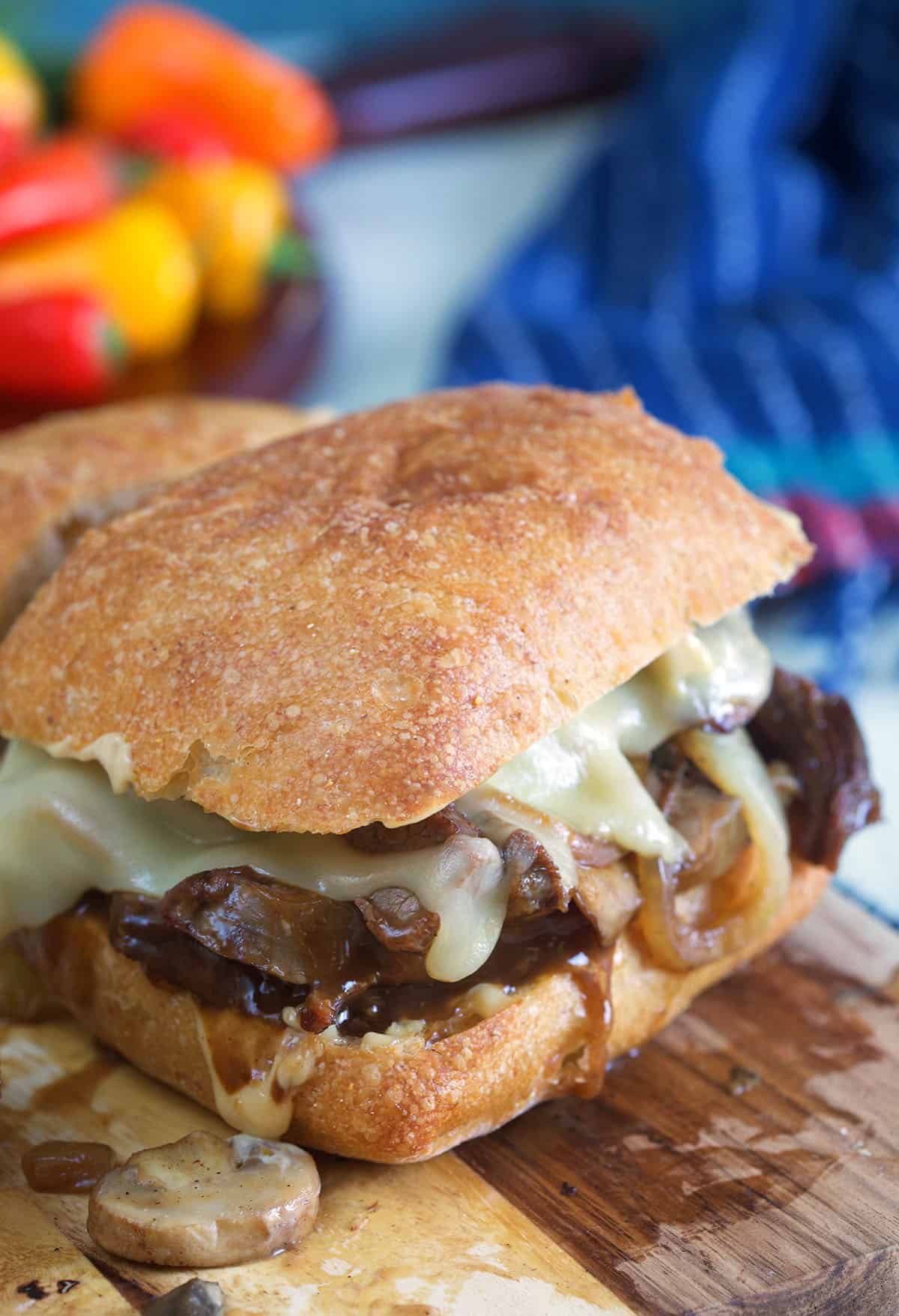 A cooked roast beef sandwich with cheese is placed on a wooden cutting board.