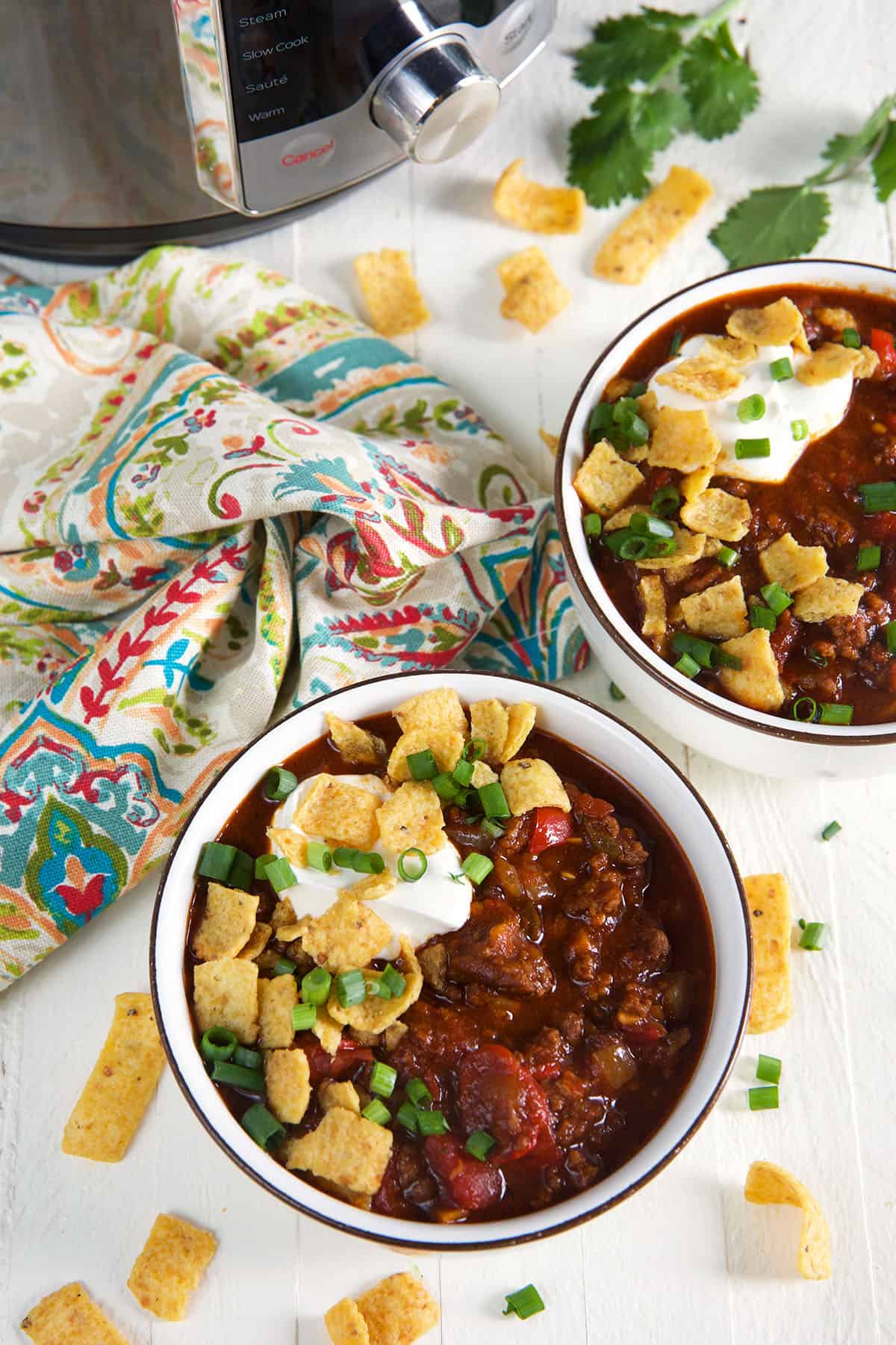 Two full, garnished bowls of chili are placed next to a tea towel and the Instant Pot.