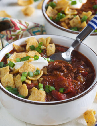 A bowl of chili is topped with fritos, sour cream, and green onions.