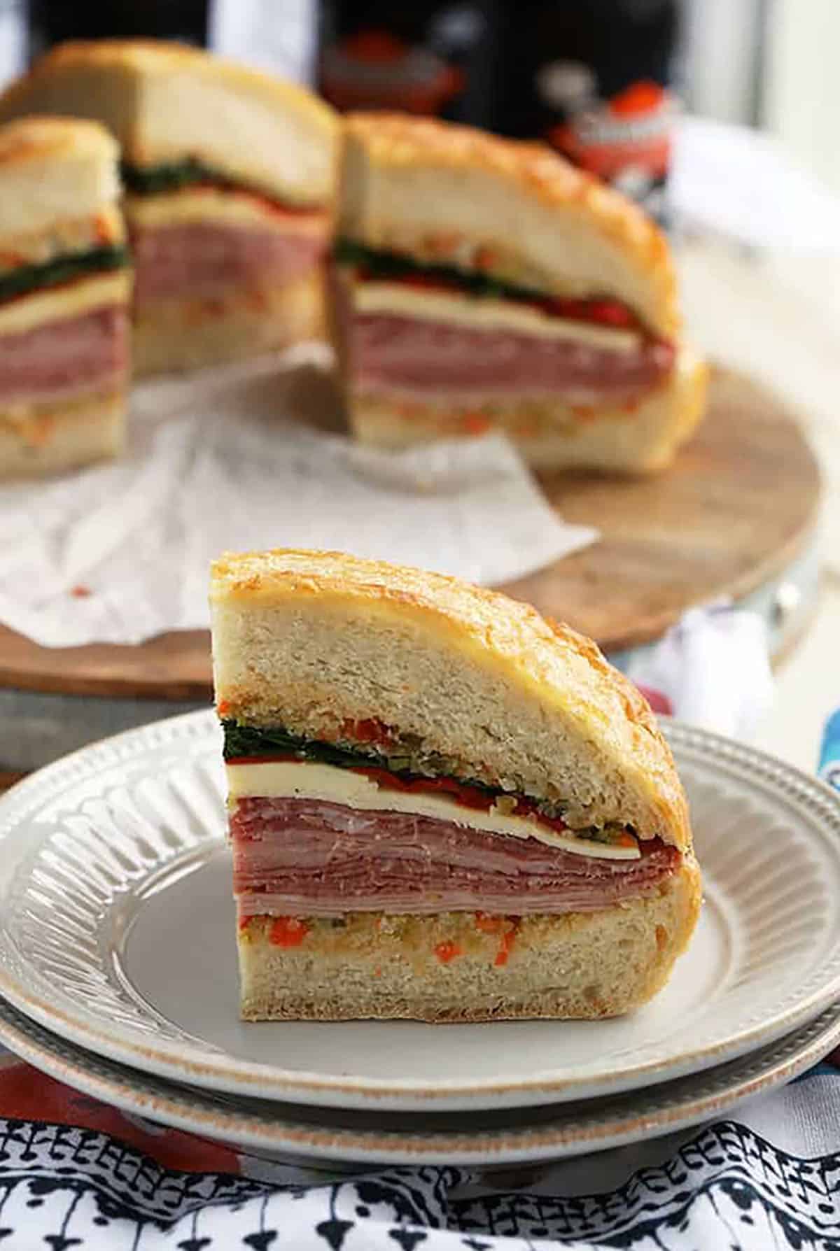 Wedge of a Muffuletta Sandwich on a white plate with other slices behind it.