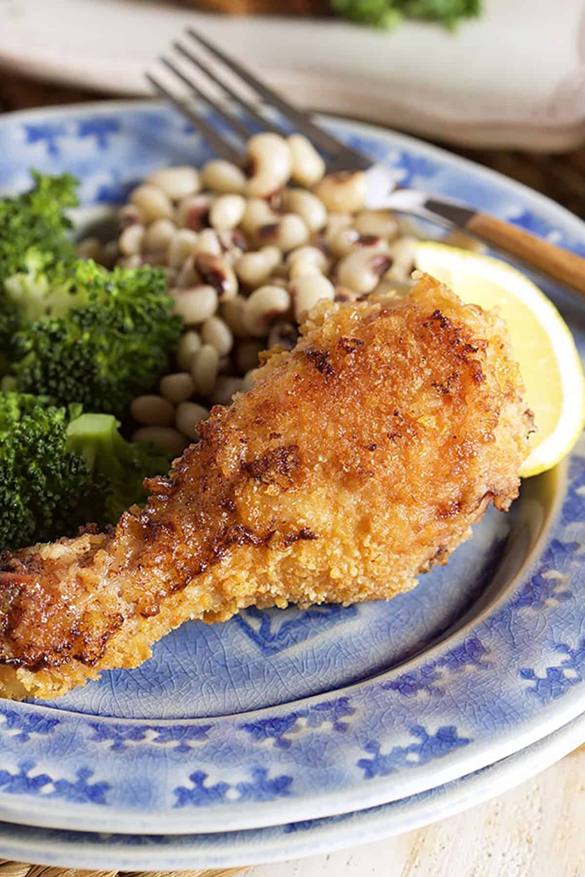 Oven Fried Chicken drumstick on a blue plate with black eyed peas and broccoli.