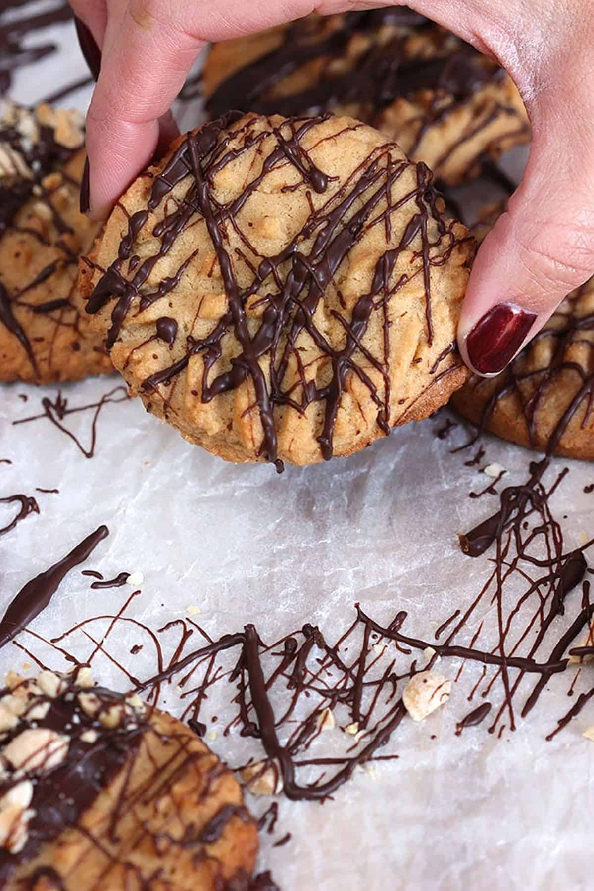 Peanut butter cookie drizzled with chocolate being lifted from a sheet of parchment paper