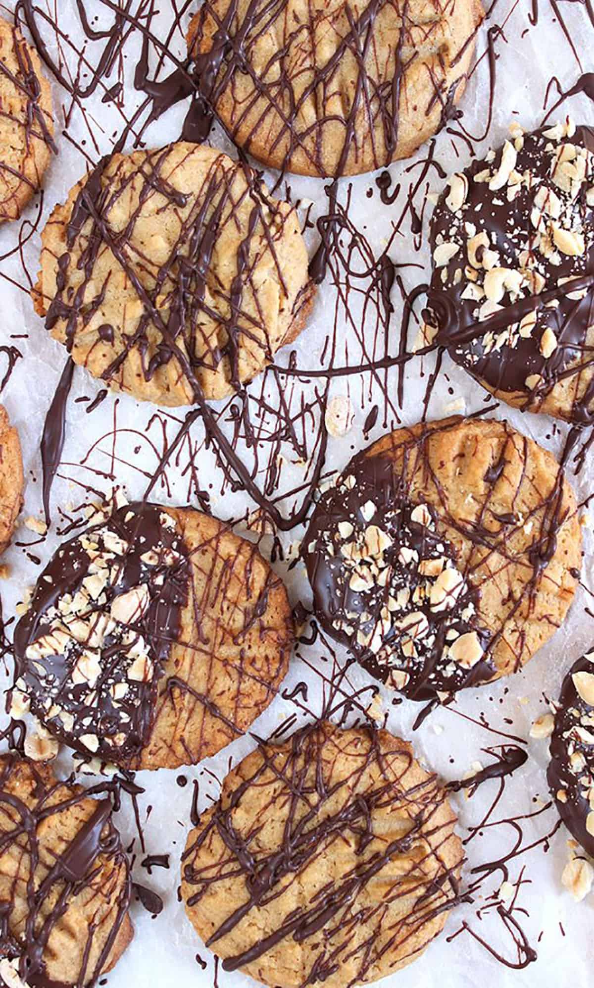 Peanut butter cookies on a sheet of parchment drizzled with chocolate.