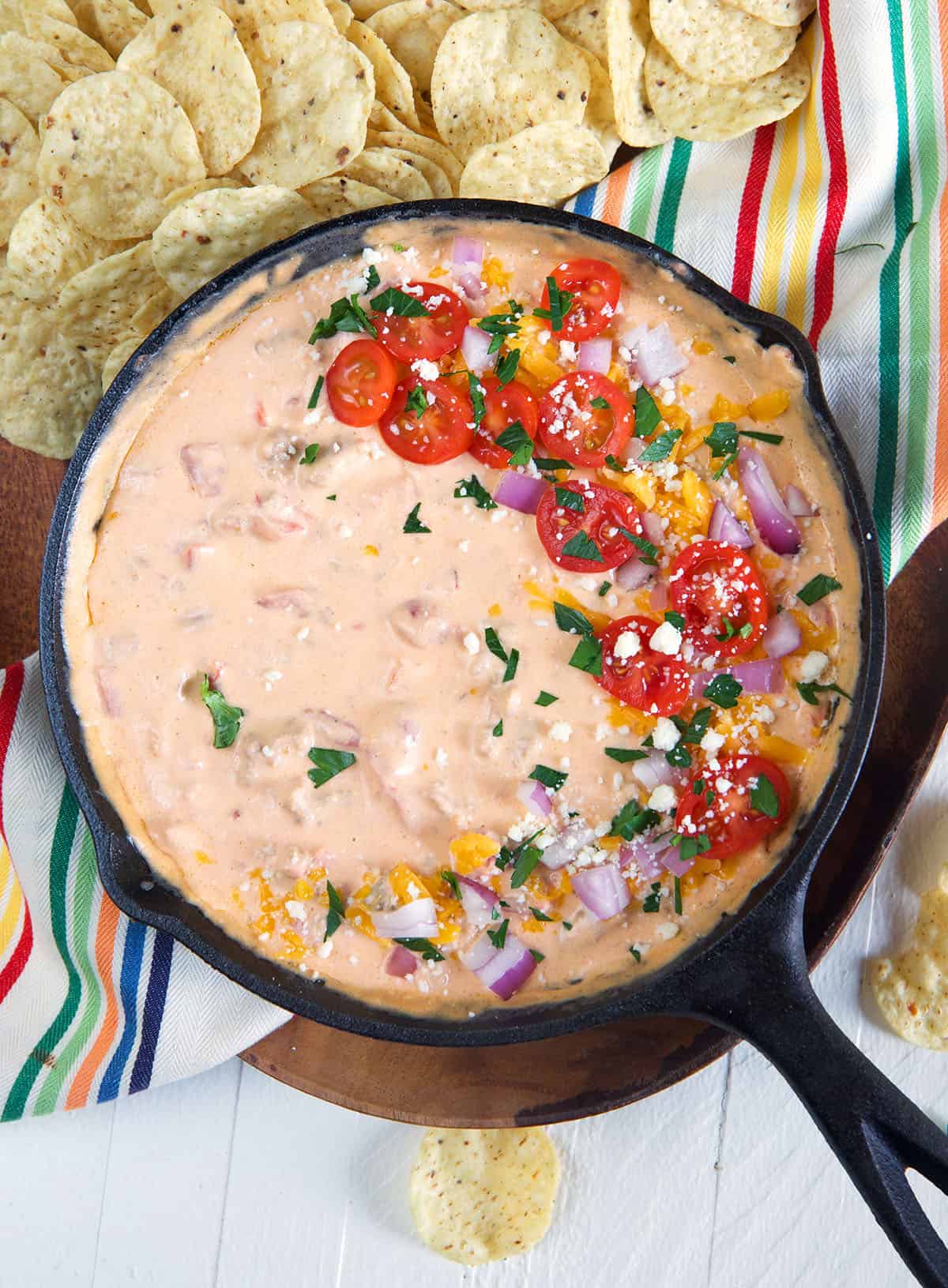 A black skillet is filled with rotel dip and topped with tomatoes, red onions, and green onions.