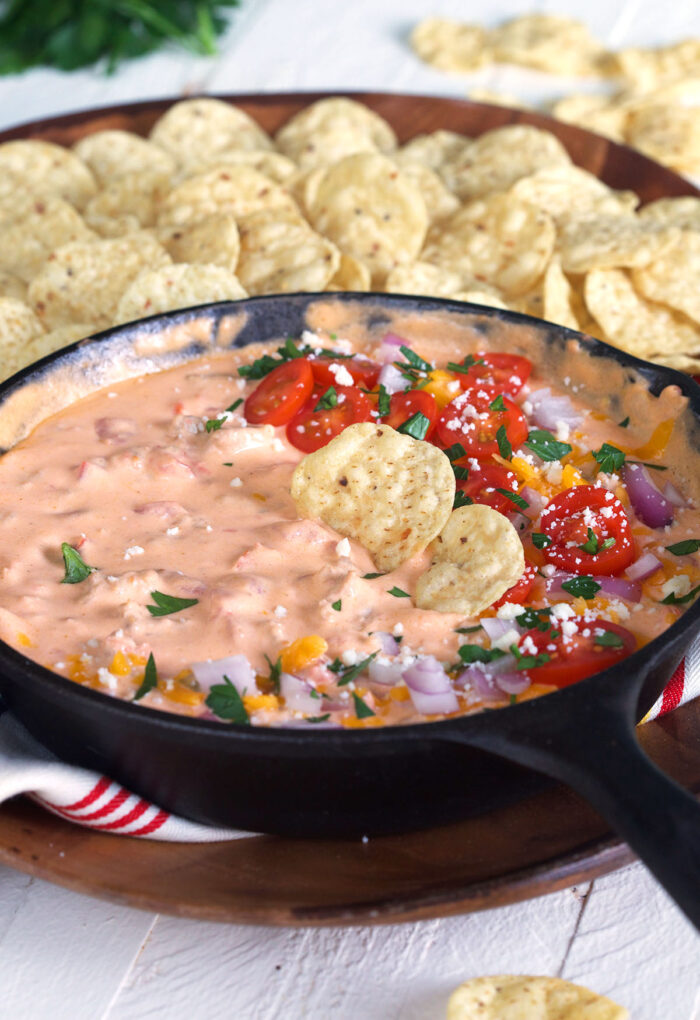 A skillet filled with cheese dip is placed next to a large serving of tortilla chips.