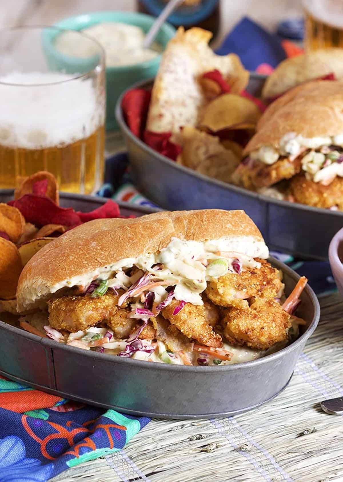 Shrimp Po Boy Sandwich in a steal tray with a glass of beer in the background.
